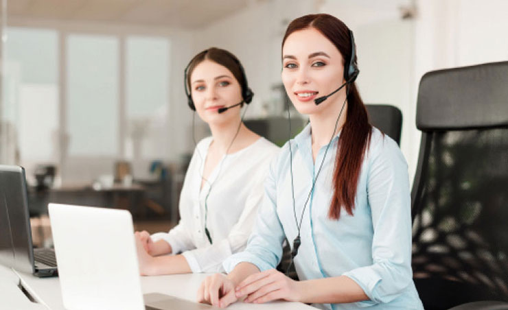Eine freundliche Mitarbeiterin sitzt an einem Schreibtisch mit Headset, bereit, Anfragen zur Rekrutierung von Pflegekräften entgegenzunehmen.