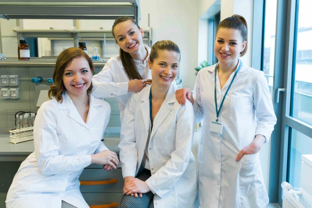Ein Team junger Pflegekräfte in weißen Kitteln, die in einem modernen Raum gemeinsam lächeln und sich austauschen.
