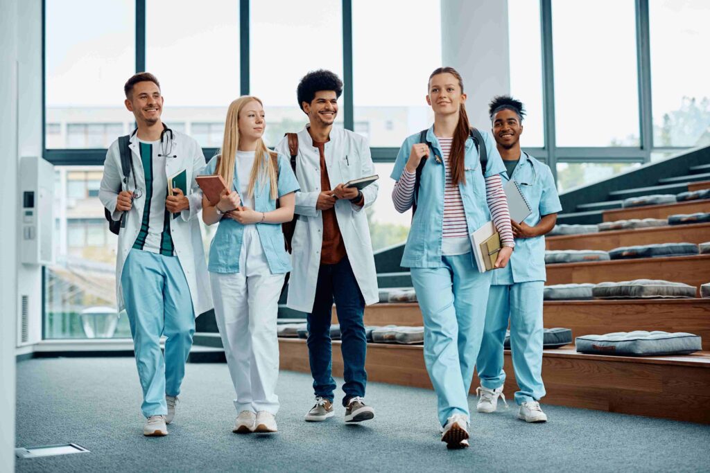 Eine Gruppe junger Pflegekräfte und Medizinstudenten in blauer Uniform und Kitteln, die gemeinsam durch ein modernes Gebäude gehen.