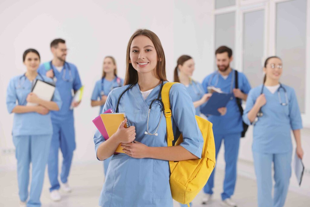 Junge Pflegekraft in blauer Uniform mit gelbem Rucksack, begleitet von weiteren Pflegekräften, bereit für ihren Einsatz in einem Krankenhaus.