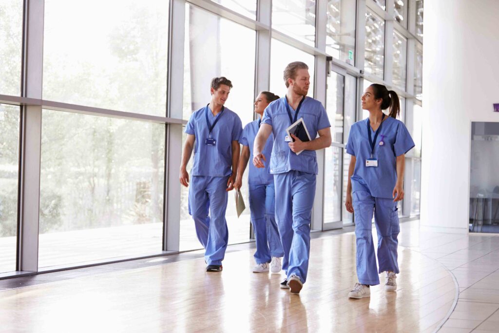 Eine Gruppe aus Pflegekräften in blauer Uniform, die gemeinsam durch ein modernes Krankenhaus geht, unterstützt durch DIH PflegeDirekt.