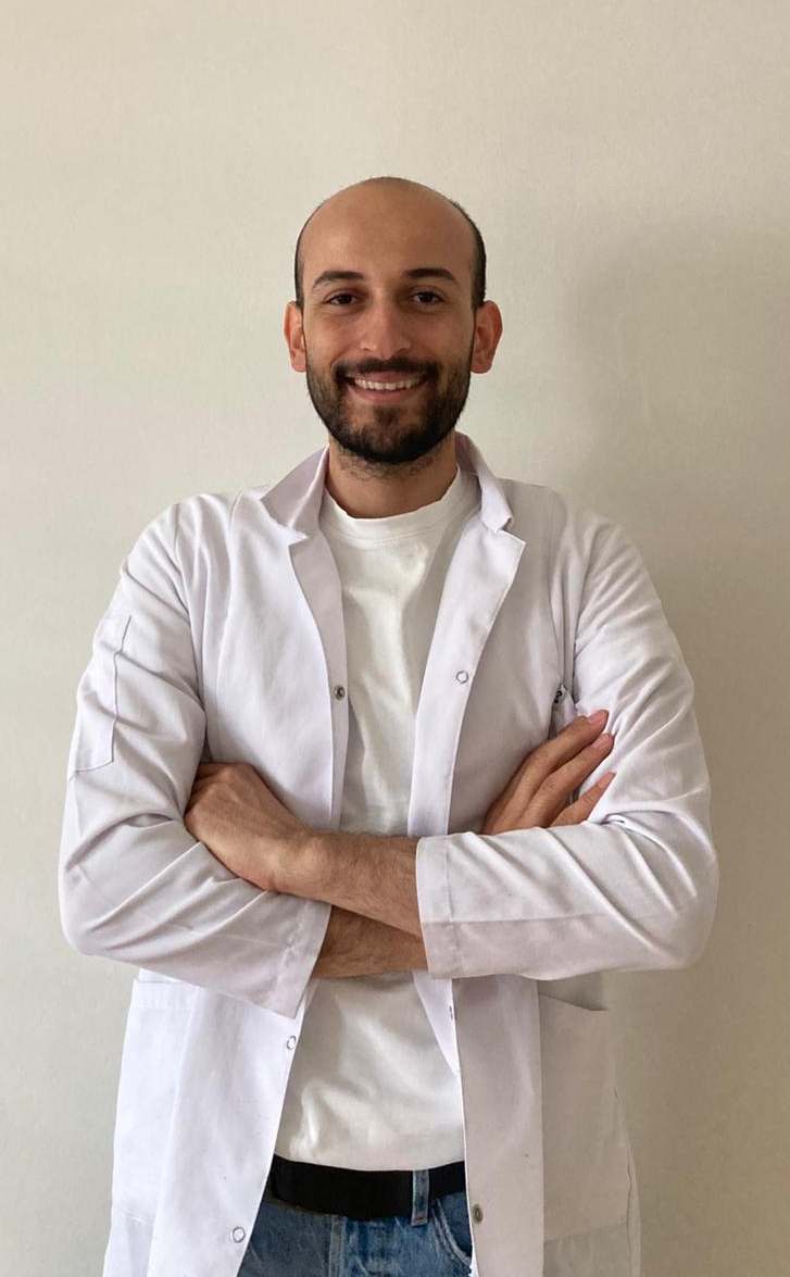 Physiotherapeut Dogukan im weißen Kittel, lächelnd mit verschränkten Armen – erfolgreicher Start in einer Praxis in Hannover.