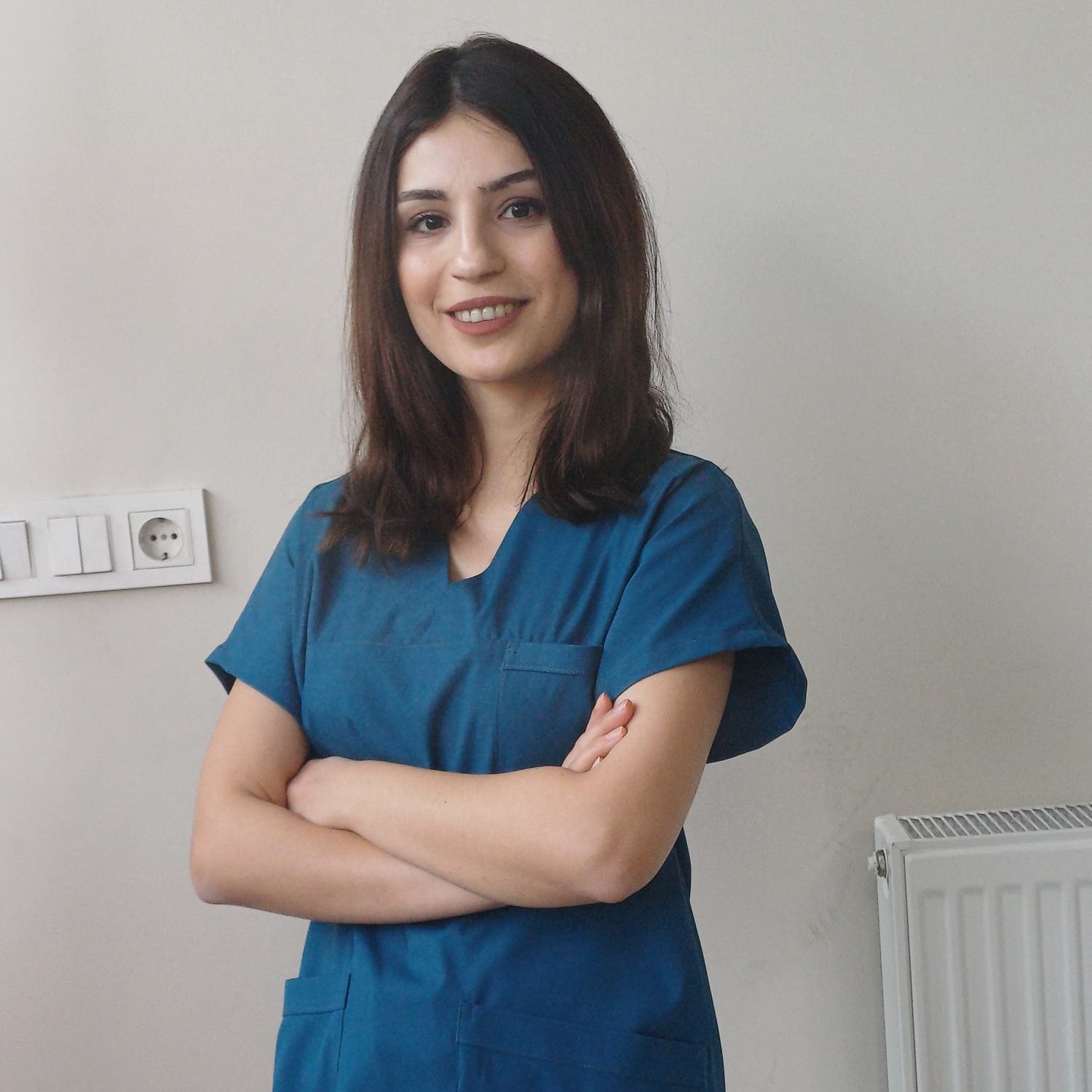 Physiotherapeutin Elif in blauer Arbeitskleidung, lächelnd mit verschränkten Armen – erfolgreicher Start in Buttenwiesen mit DIH ProPhysio.