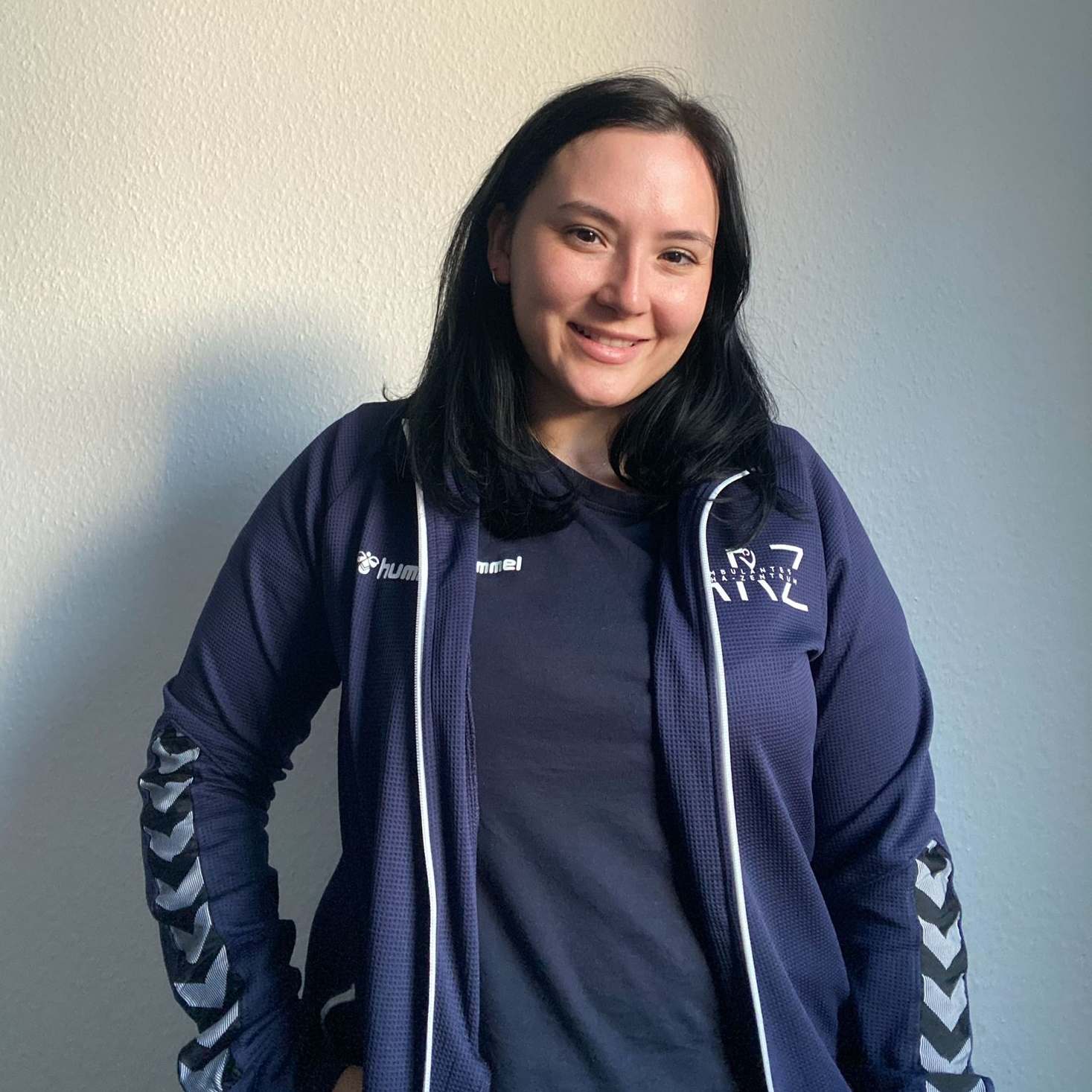 Physiotherapeutin Ecem in Sportjacke, lächelnd vor heller Wand – erfolgreicher Start als Physiotherapeutin in Walsrode.