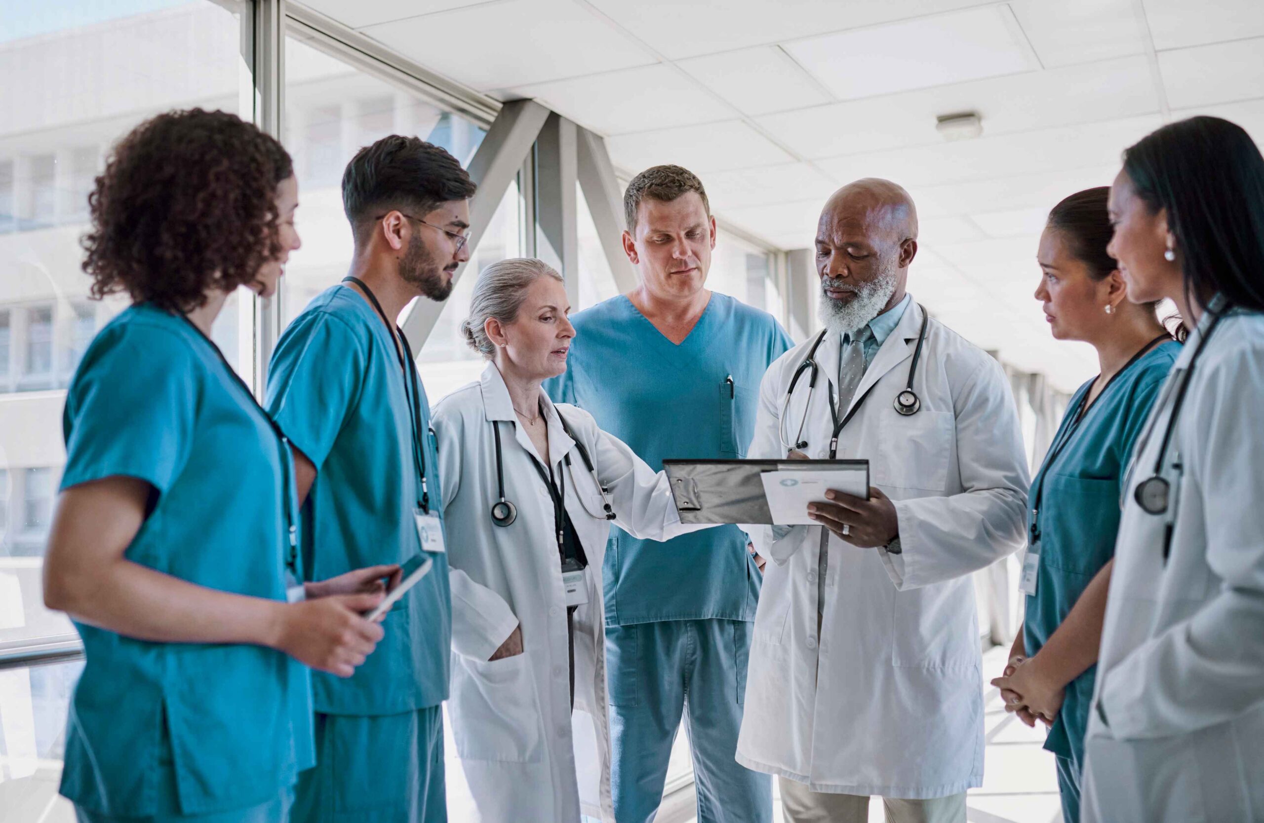 Team-Besprechung im Krankenhausflur: Ärzte und Pflegefachkräfte im Gespräch – Pflegekräfte aus dem Ausland für Kliniken